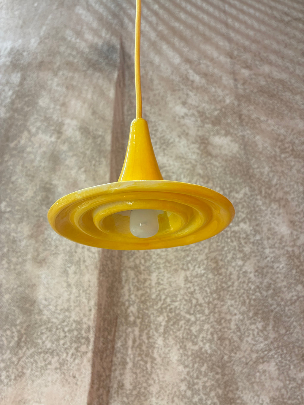 Suspension Ondine Jaune Soleil vue de dessous, avec reliefs circulaires en céramique et ampoule visible. 