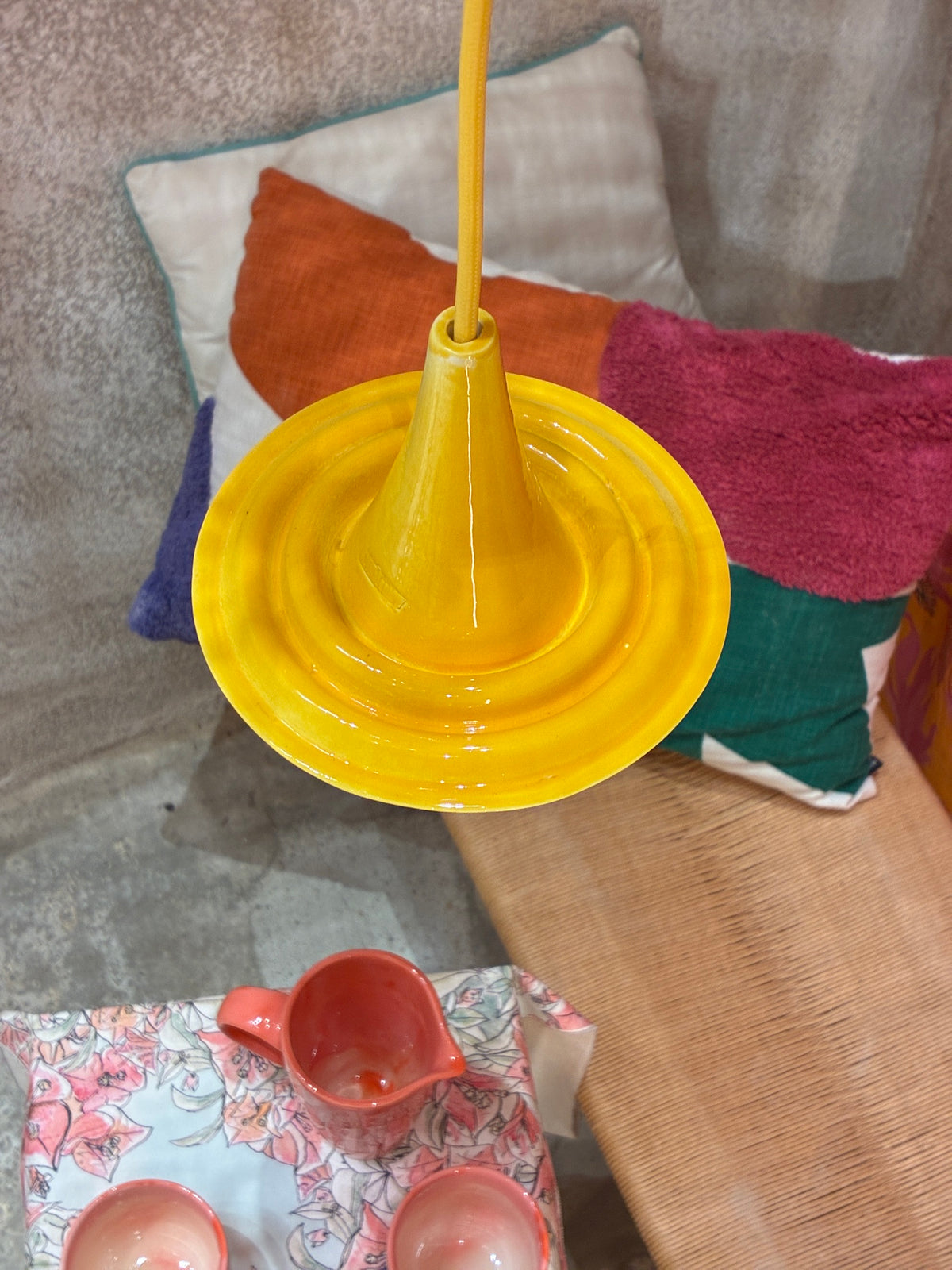 Suspension Ondine en céramique jaune vue de dessus, près de coussins colorés.