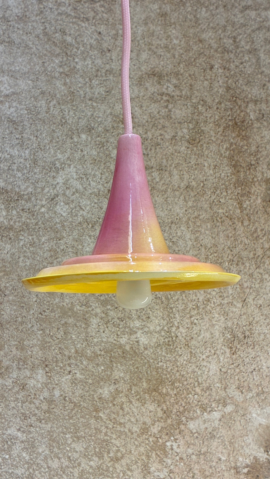 Suspension Ondine rose et jaune avec câble rose, vue légèrement de dessous avec ampoule visible. 