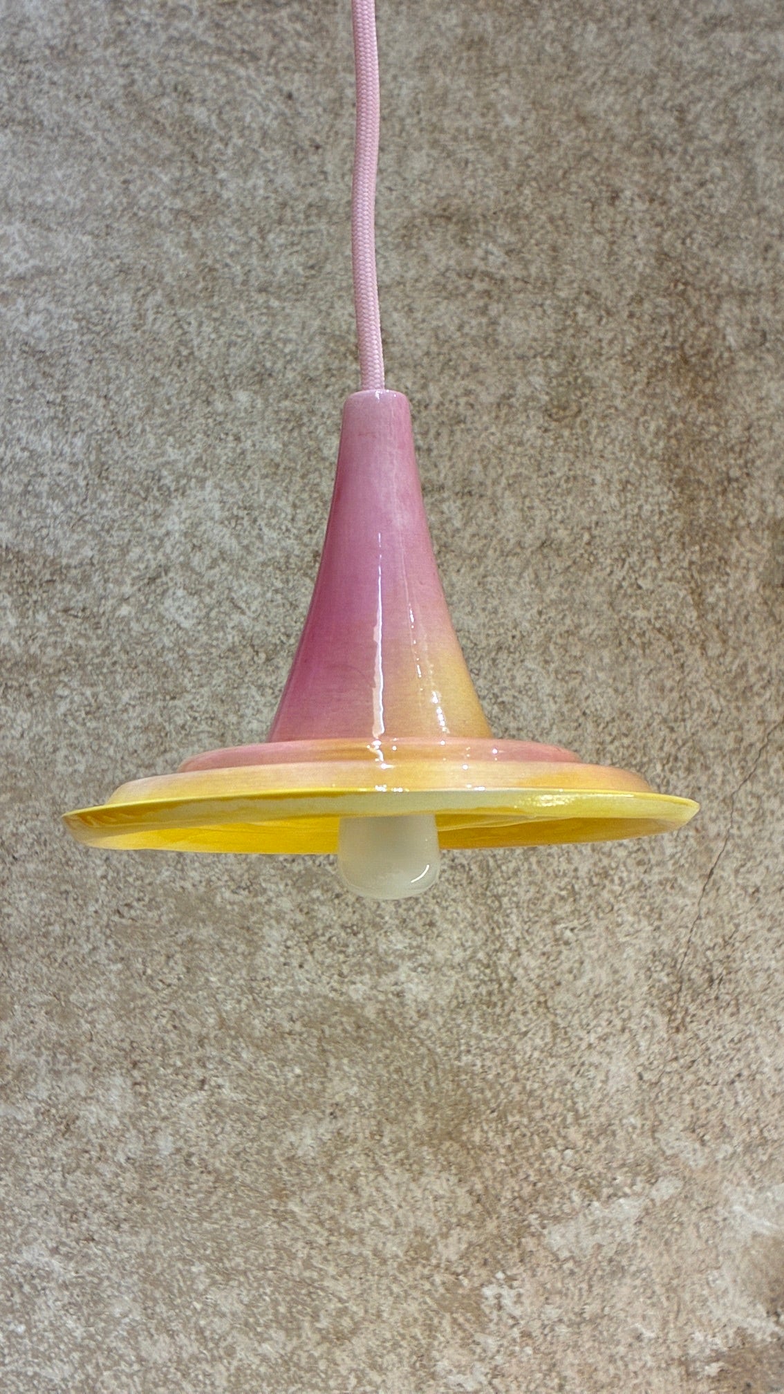 Suspension Ondine rose et jaune avec câble rose, vue légèrement de dessous avec ampoule visible. 