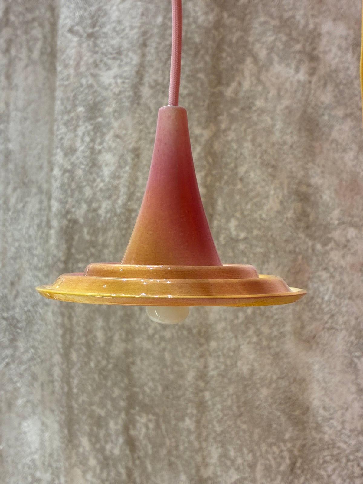 Petite suspension Ondine Rose Grasse et Jaune Soleil vue de profil devant un mur gris texturé.