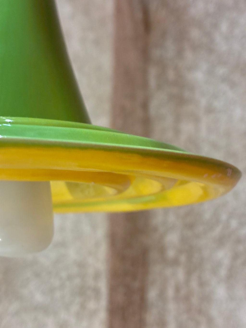 Gros plan sur le bord vert et le dessous jaune émaillé de la suspension Ondine, avec ampoule visible. 
