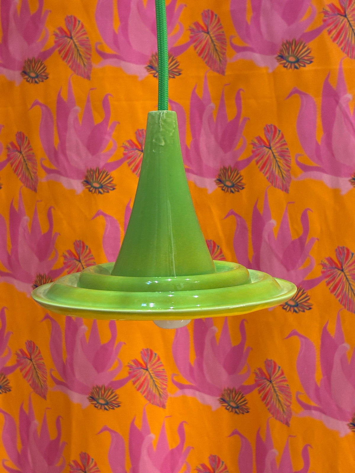 Suspension Ondine Vert Provence et Jaune Soleil avec câble vert devant un fond à motifs roses et orange.