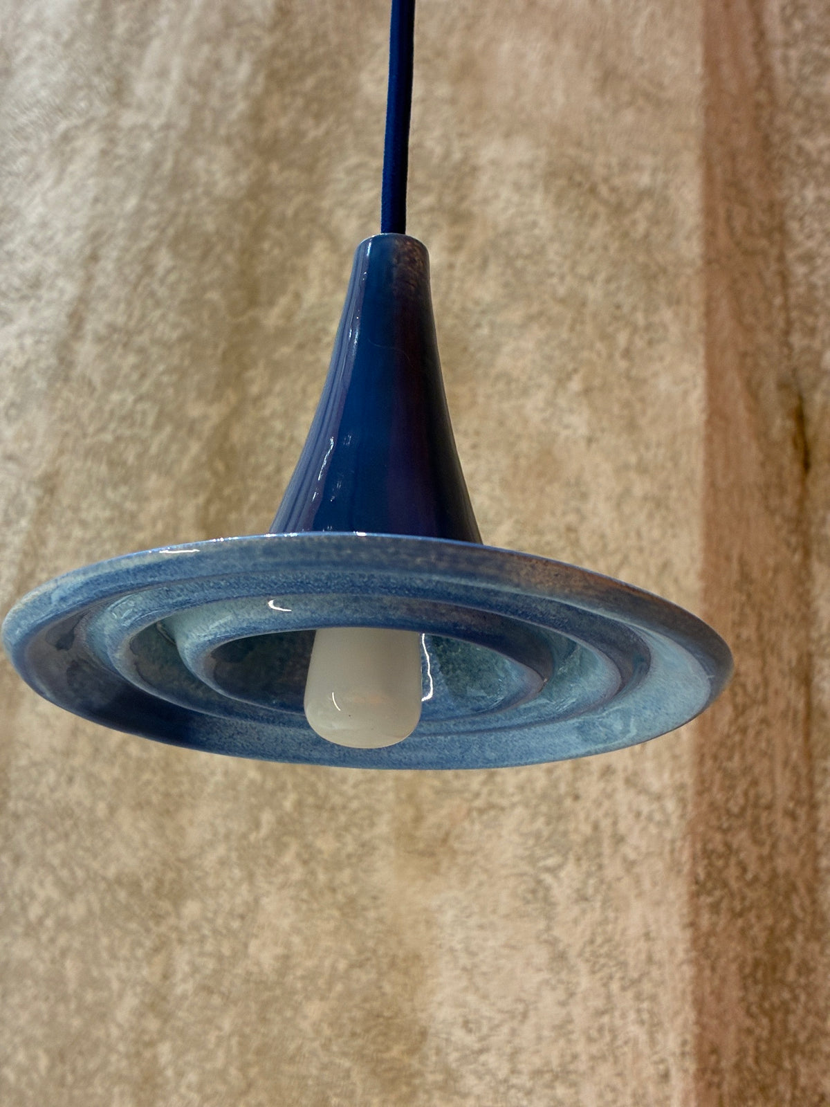  Suspension Ondine bleue vue de dessous, avec ampoule visible et reliefs circulaires. 