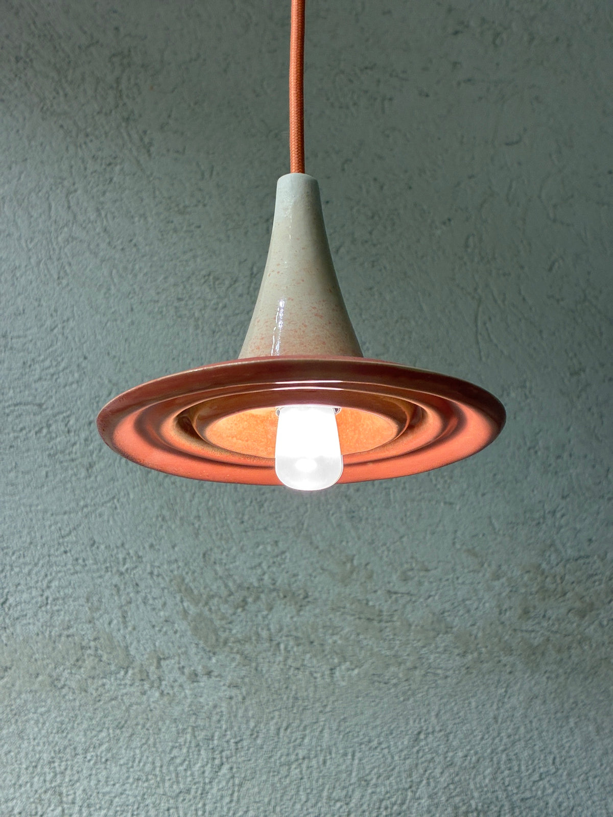 Suspension Ondine rose et beige allumée, vue de dessous avec ampoule et reliefs circulaires visibles